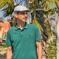 Man wearing a green polo shirt and beige Men’s lightweight summer newsboy cap standing outdoors with palm trees in the background