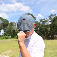 man in Blue Silk Newsboy. Italian summer hat with landscaping in background
