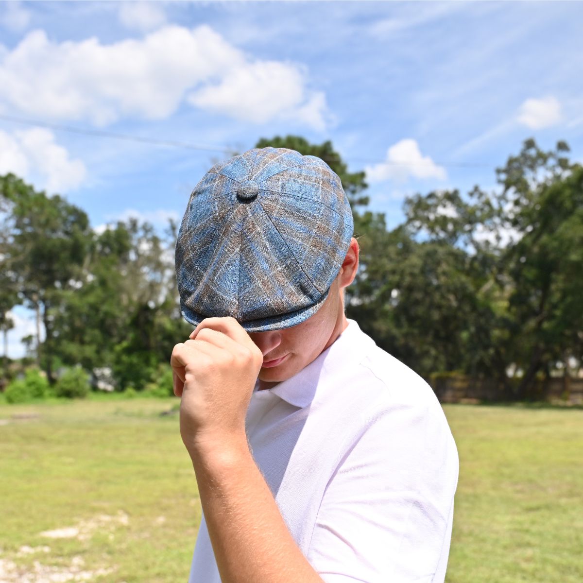 man in Blue Silk Newsboy. Italian summer hat with landscaping in background
