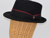 Black alpine hat displayed on a wicker mannequin head, featuring a structured crown, a black ribbon band with a burgundy stripe, and a metallic floral pin detail.