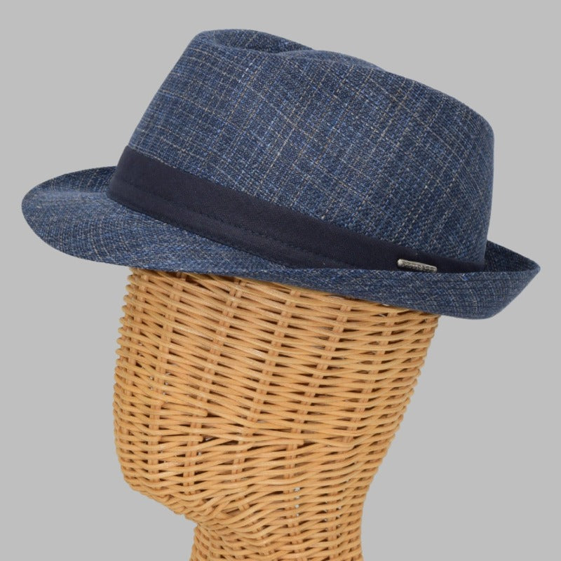 This image features a stylish Alpine fantasy hat on mannequin, made from a light, textured fabric with a blue band around the crown. It has a classic shape, with a slightly curved brim and a subtle logo on the side. The hat's neutral color and sophisticated design make it suitable for a variety of occasions.