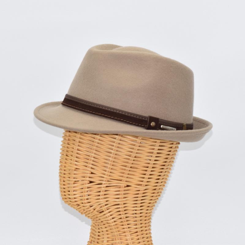 Side view of a beige alpine hat displayed on a wicker mannequin head, featuring a brown leather band with metallic accents for a sophisticated touch.