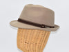 Side view of a beige alpine hat displayed on a wicker mannequin head, featuring a brown leather band with metallic accents for a sophisticated touch.