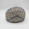 A beige flat cap with a blue plaid pattern, viewed from the back, showcasing the symmetrical stitching and classic design.