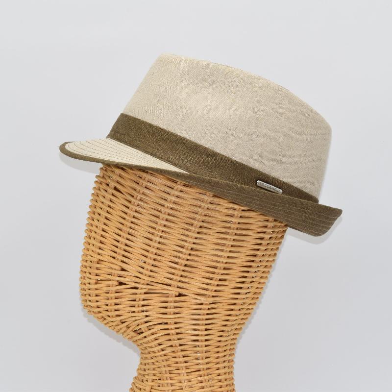 Side view of a beige alpine hat with a structured crown, a brown ribbon band, and a matching brim, displayed on a wicker mannequin head with a metallic logo detail.