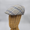  A beige flat cap with a blue plaid pattern displayed on a wicker mannequin head, showcasing its side profile and structured design.