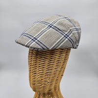  A beige flat cap with a blue plaid pattern displayed on a wicker mannequin head, showcasing its side profile and structured design.