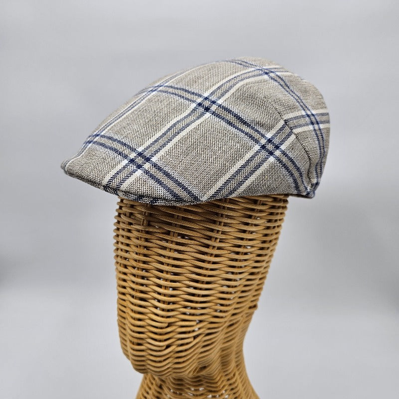  A beige flat cap with a blue plaid pattern displayed on a wicker mannequin head, showcasing its side profile and structured design.