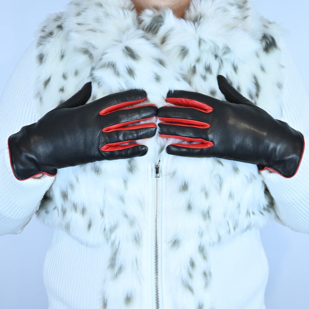 A pair of black leather gloves with bold red accents between the fingers and trim, worn by a person dressed in a white fur-patterned jacket.