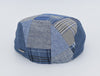 The back view of a blue patchwork driver cap made from an assortment of denim and patterned fabrics, including plaid and herringbone designs. The cap's rounded crown and meticulous stitching create a stylish and contemporary look. A small metallic detail is visible on the side, adding a touch of sophistication.