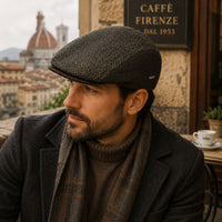 A man wearing a Brown Lucca Driver Cap, a brown turtleneck sweater, and a brown plaid scarf, sitting at a cafe with a sign that reads 'CAFFÈ FIRENZE DAL 1953' and the Florence Duomo in the background.
