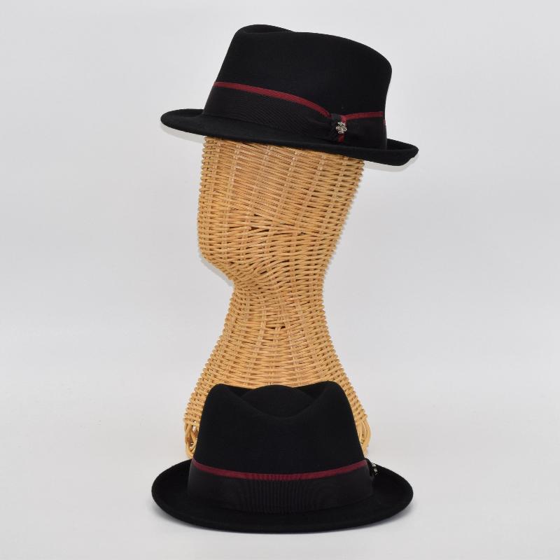 Two black alpine hats with burgundy-accented ribbon bands, one displayed on a wicker mannequin head and the other resting flat, showcasing their elegant design and structured crown