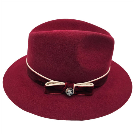 Luxurious burgundy felt fedora with a wide brim, adorned with a velvet band, cream piping, and an elegant bow featuring a decorative metallic emblem, combining classic style with refined detailing.