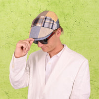 Person wearing a patchwork cap and sunglasses against a green textured background