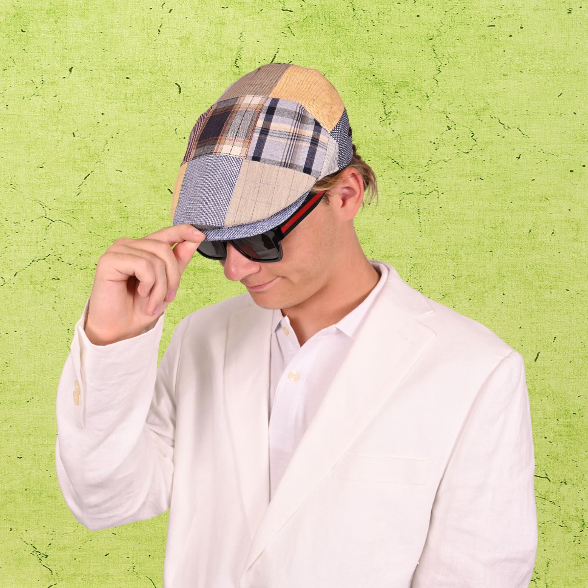 Person wearing a patchwork cap and sunglasses against a green textured background