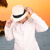 Person wearing a white shirt and Panama hat by a body of water with a sunset in the background