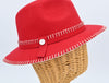 A bright red felt fedora hat with white decorative stitching along the brim and crown, featuring a red ribbon band with a small metallic button detail