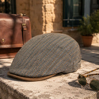 A Gray Lozo Flat Cap, resting on a stone ledge outdoors next to sunglasses and a brown leather bag.