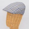 A gray flat cap with a blue and white plaid pattern, displayed on a wicker mannequin head, highlighting its structured side profile and classic style.