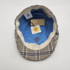 The interior of a beige flat cap with a blue plaid pattern, featuring a light blue lining, "Petracci" branding, and a tag indicating "Made in Italy."