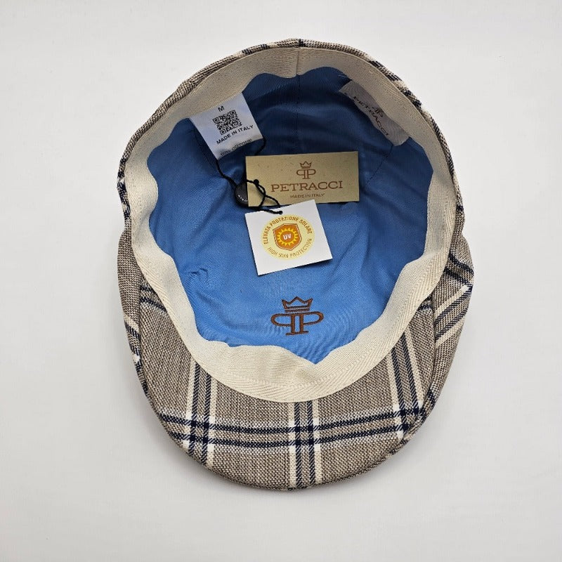 The interior of a beige flat cap with a blue plaid pattern, featuring a light blue lining, "Petracci" branding, and a tag indicating "Made in Italy."