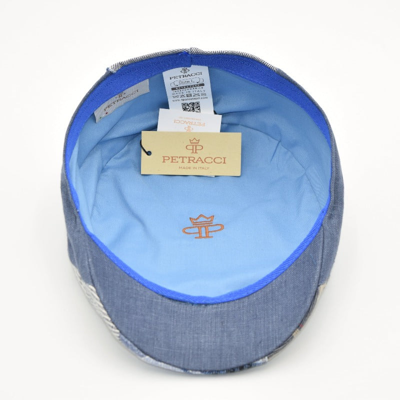 The interior of an Italian-made ivy cap with a luxurious blue lining featuring the "Petracci" logo embroidered in orange. The cap showcases precise craftsmanship, with labels and tags highlighting its authenticity and origin. The patchwork denim design on the outer edge complements the smooth, tailored interior.