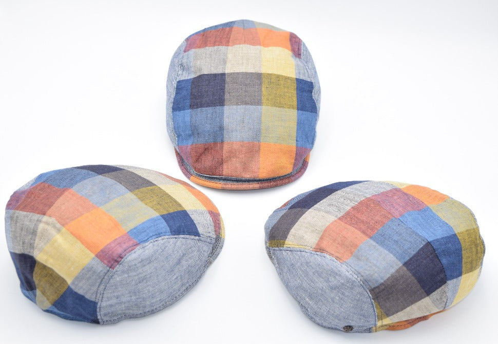 Three multicolored patchwork flat caps arranged in a triangular formation. Each cap features vibrant panels of blue, yellow, orange, and red hues, with visible herringbone patterns on some sections. The caps showcase front, side, and back views for a comprehensive display.