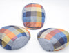 Three multicolored patchwork flat caps arranged in a triangular formation. Each cap features vibrant panels of blue, yellow, orange, and red hues, with visible herringbone patterns on some sections. The caps showcase front, side, and back views for a comprehensive display.
