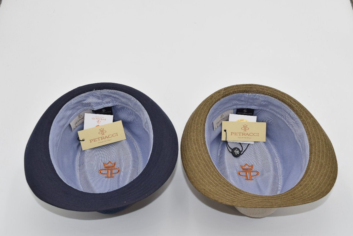 Interior view of two alpine hats, one navy and one beige with a brown brim. Both feature light blue lining, the 'Petracci' branding tag, and embroidered orange logo detail inside