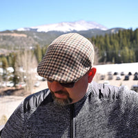 Model in beige Pied de Poule wool cap in earth-tone pattern with mountains in background