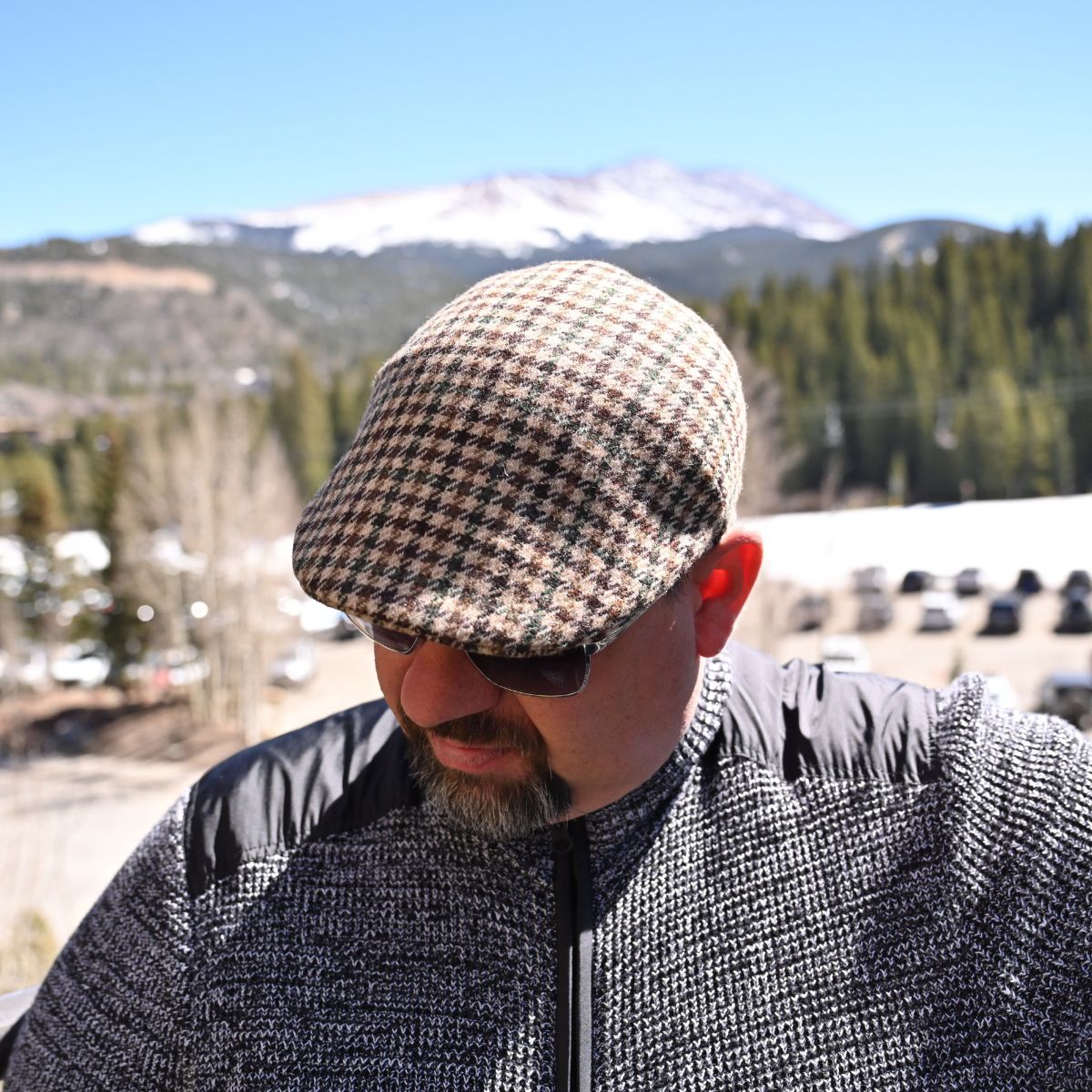Model in beige Pied de Poule wool cap in earth-tone pattern with mountains in background