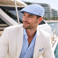 Man in Light blue Positano Linen Flat Cap with a contrasting darker blue linen visor, featuring a sleek, breathable summer design and a subtle side logo detail.