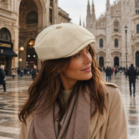 A woman wearing a creme Arezzo Italian Newsboy Hat and a taupe scarf, standing in a city square with the Milan Cathedral in the background.