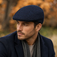 A man wearing a Blue shetland Wool Driver Cap, navy blazer, and gray scarf, photographed outdoors with a soft-focus autumn background.