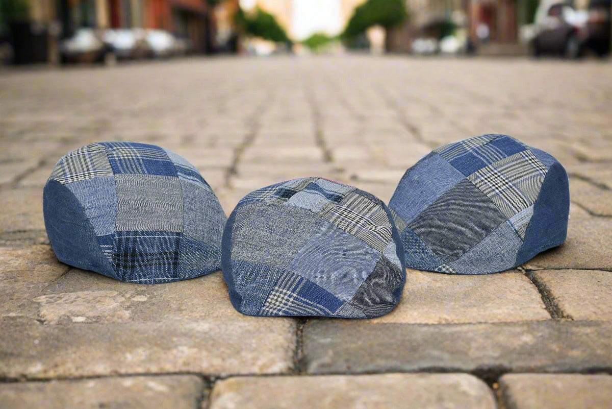 A trio of denim patchwork caps displayed on a cobblestone street, blending modern style with a classic urban backdrop. Each cap features unique blue patterns, including plaid, herringbone, and solid denim textures. The natural outdoor setting highlights the versatility and craftsmanship of these stylish headpieces.