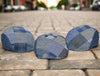 A trio of denim patchwork caps displayed on a cobblestone street, blending modern style with a classic urban backdrop. Each cap features unique blue patterns, including plaid, herringbone, and solid denim textures. The natural outdoor setting highlights the versatility and craftsmanship of these stylish headpieces.