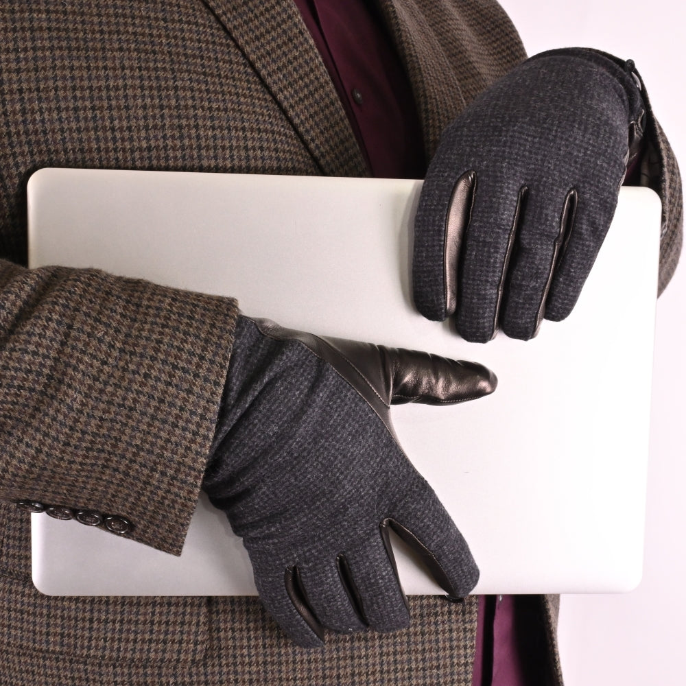 Close-up of a person wearing textured black wool gloves with leather accents, holding a laptop while dressed in a houndstooth-patterned jacket and a burgundy shirt.