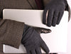 Close-up of a person wearing textured black wool gloves with leather accents, holding a laptop while dressed in a houndstooth-patterned jacket and a burgundy shirt.